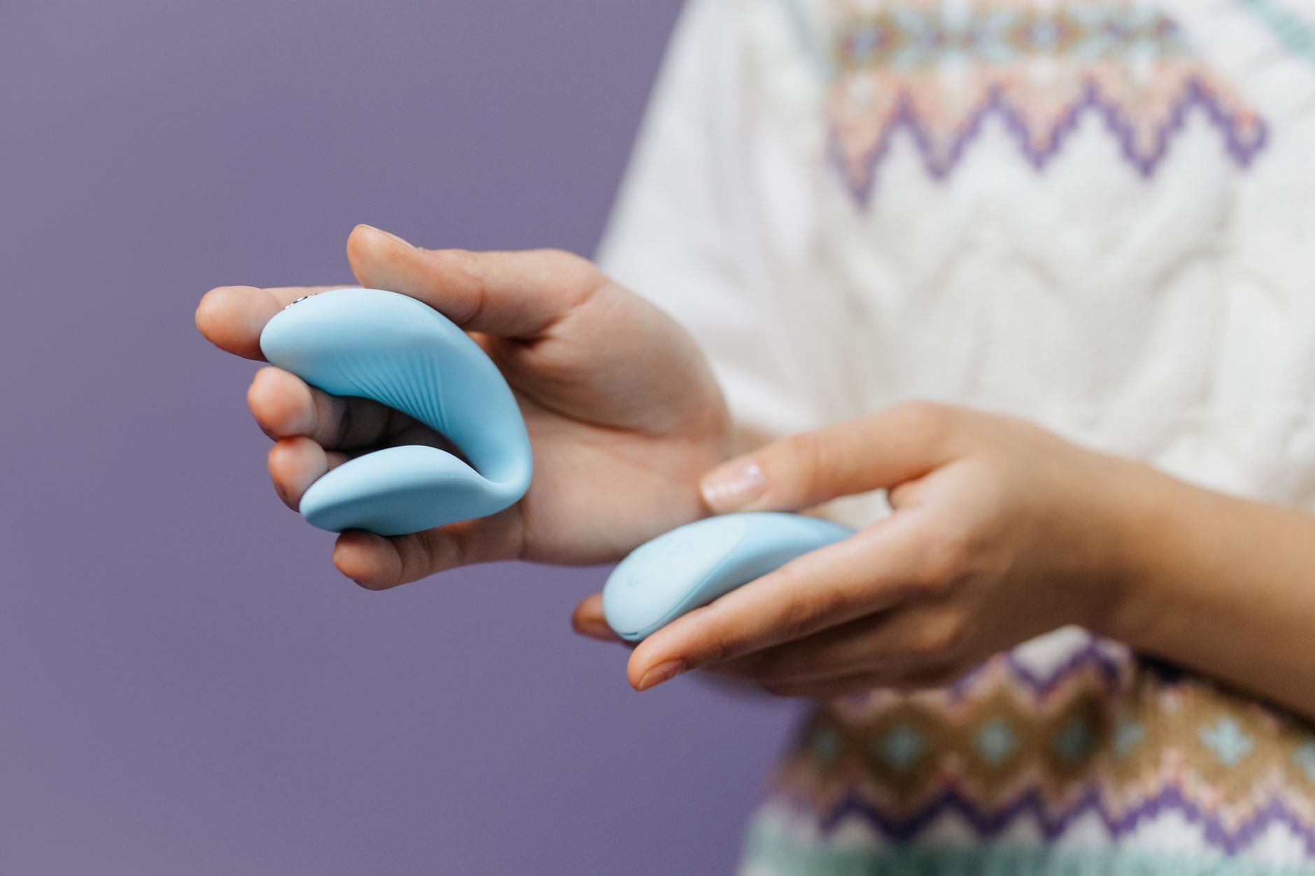 Hand reaching over a collection of colorful vibrators and sex toys arranged on a surface