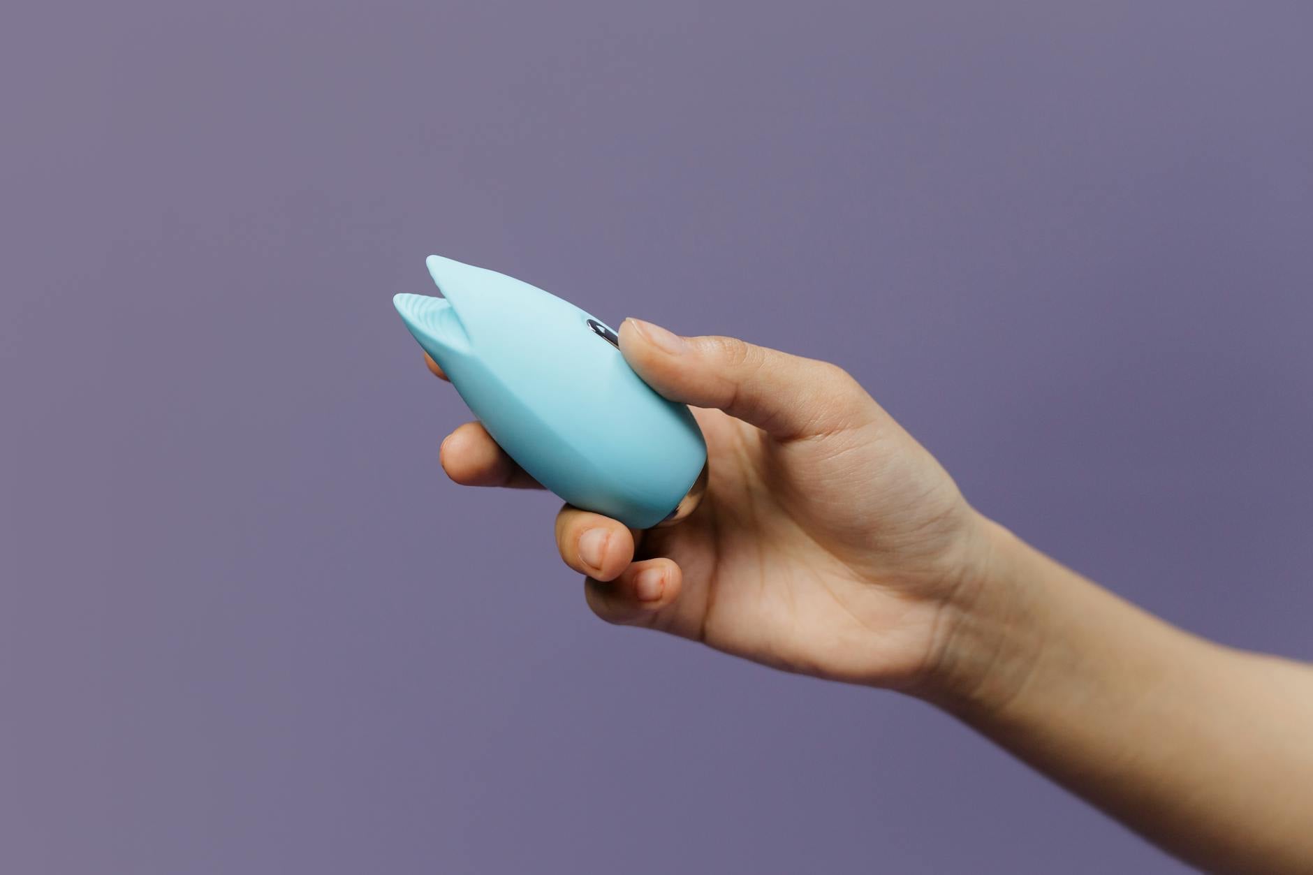 A blue silicone vibrator held in hand against a purple background, highlighting personal pleasure and self-care