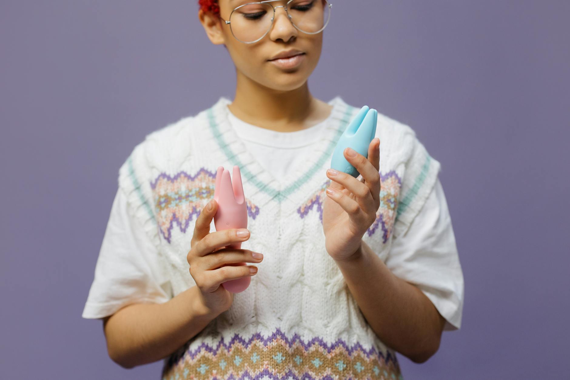 Woman holding blue and pink silicone vibrators in a thoughtful pose, exploring sensation recovery options